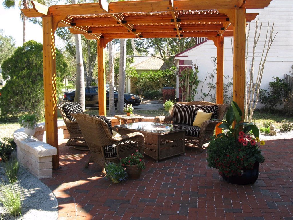 Resimde, ahşap bir pergolanın altında rattan mobilyalarla döşenmiş, tuğla döşeli şık bir oturma alan Resimde, ahşap bir pergolanın altında rattan mobilyalarla döşenmiş, tuğla döşeli şık bir oturma alanı görülmektedir. Bahçe düzenlemesi ve bitki saksıl