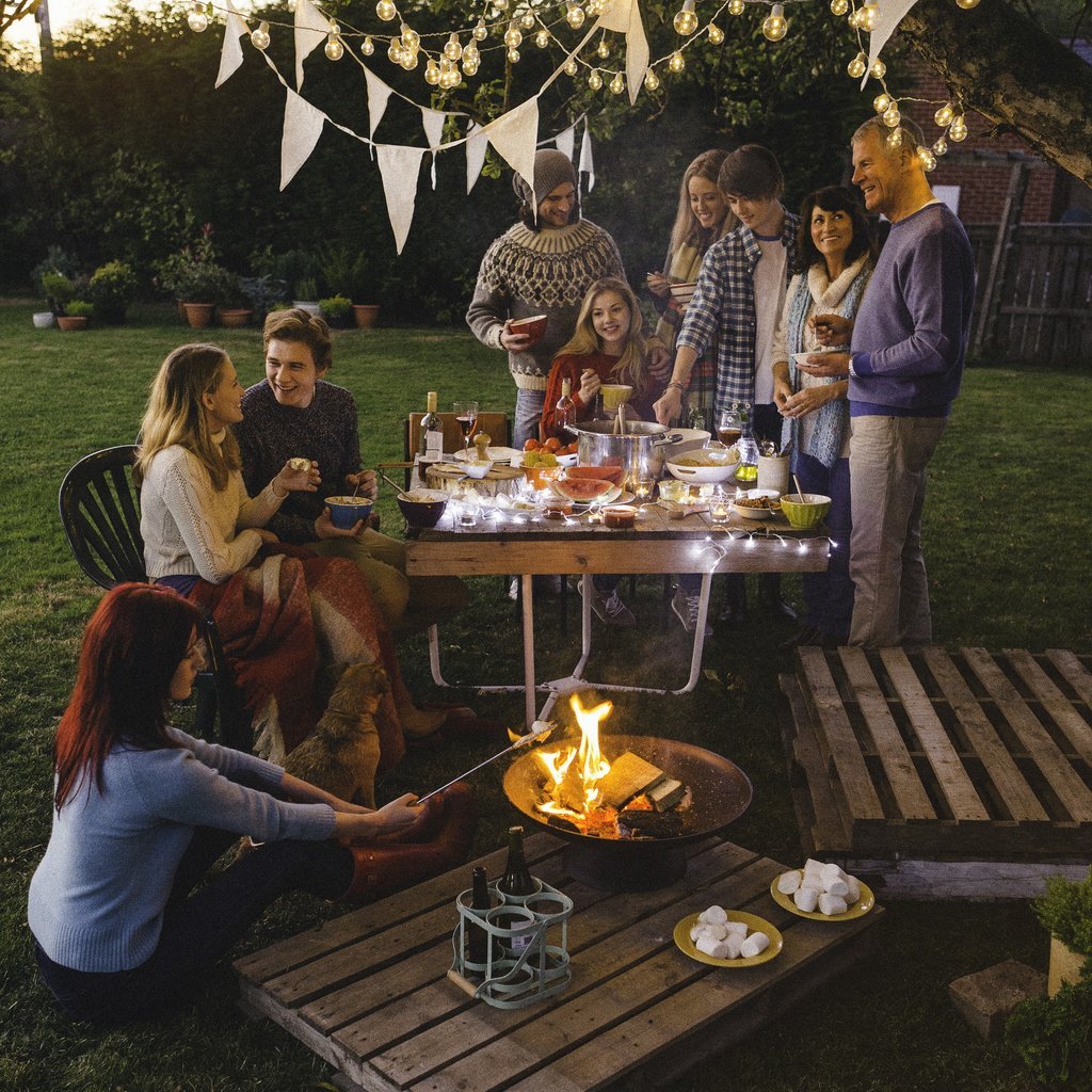 Bahçede ateş başında toplanmış bir grup insanın keyifli anları yansıtan bu fotoğraf, sıcak ve samimi bir atmosfer sunuyor. Akşam yemeği ve marshmallow