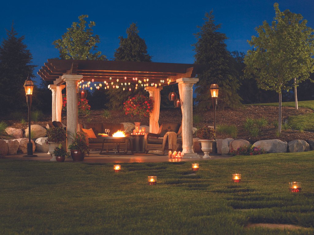Akşam vakti, bahçede pergolanın altında yanan ateş ve mumlarla romantik bir atmosfer oluşturulmuş. B Akşam vakti, bahçede pergolanın altında yanan ateş ve mumlarla romantik bir atmosfer oluşturulmuş. Bahçe aydınlatması ve peyzaj düzenlemesiyle huzurlu