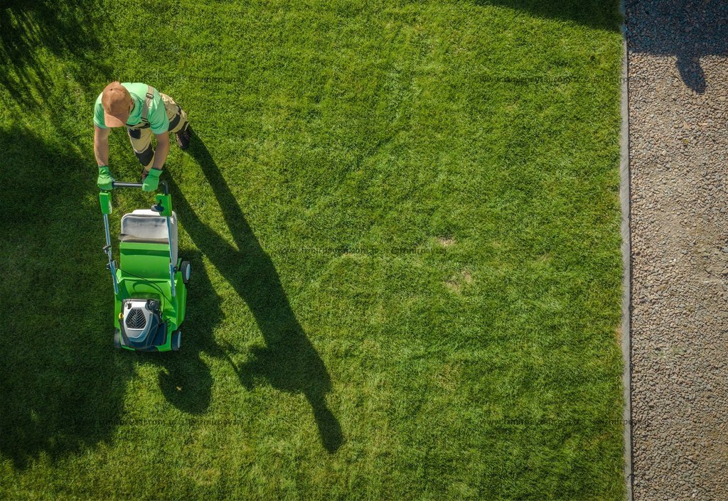 Yukarıdan çekilmiş bu fotoğrafta, çim biçme makinesiyle çimleri düzenleyen bir bahçıvan görülüyor. Yeşil çimler ve bahçıvanın gölgesi, doğal bir atmos
