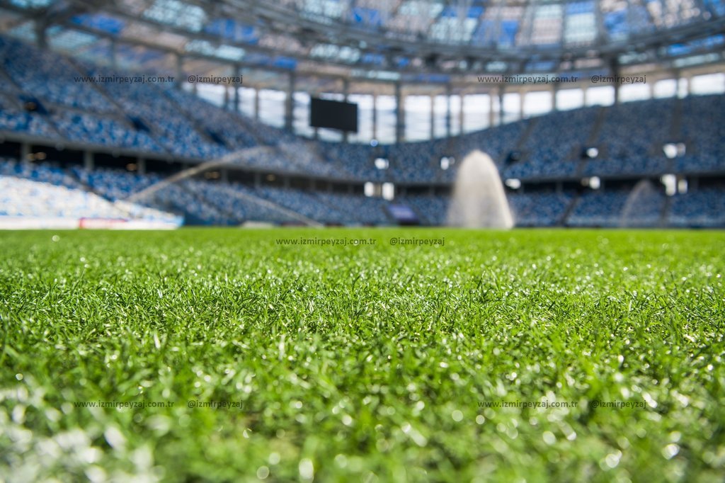 Futbol sahasının yemyeşil çimleri ve stadyumun mavi koltukları ile dikkat çeken bir görüntü. Profesyonel bir futbol maçı için hazır olan stadyumun atm