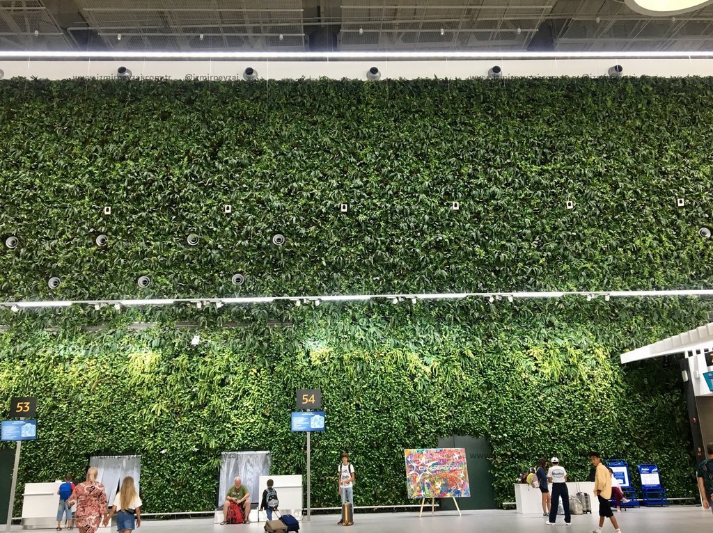 İzmir Adnan Menderes Havalimanı'nda bulunan dikey bahçe duvarı, yolculara doğal bir atmosfer sunuyor. Yeşil bitki örtüsüyle kaplı bu duvar, havalimanı