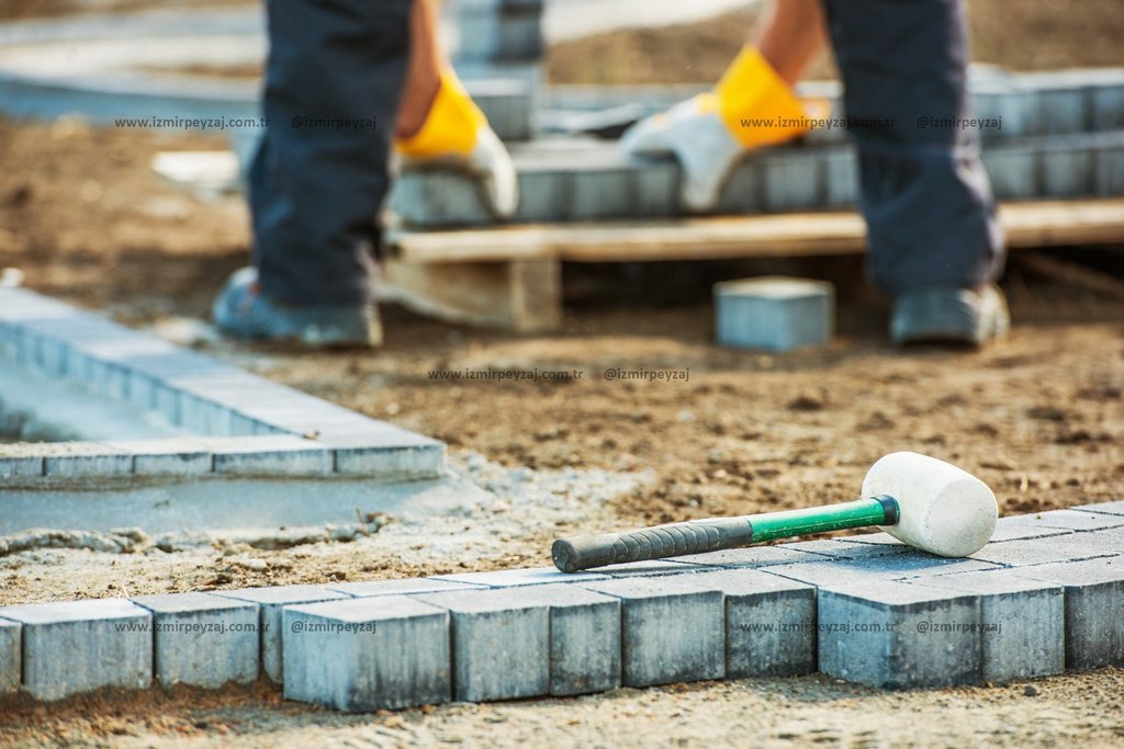 İnşaat işçileri tarafından parke taşı döşeme işlemi sırasında kullanılan beyaz başlıklı bir tokmak ve döşenmiş parke taşları görülmektedir. Zemin düze