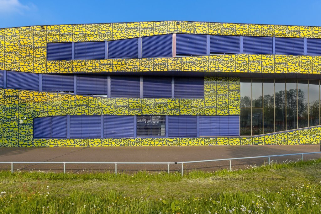 Sarı ve mavi renklerdeki modern bir binanın dış cephesi, dikkat çekici deseniyle öne çıkıyor. Bina, mimari tasarımı ve renk kombinasyonuyla çağdaş bir